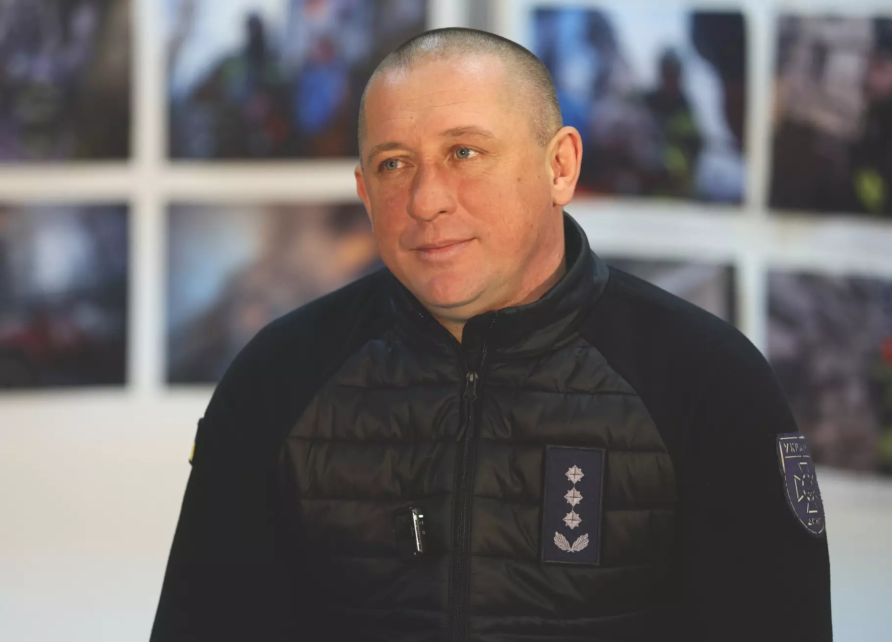 Чоловік у чорній куртці на фоні фотографій, пов'язаних з рятувальними операціями ДСНС України