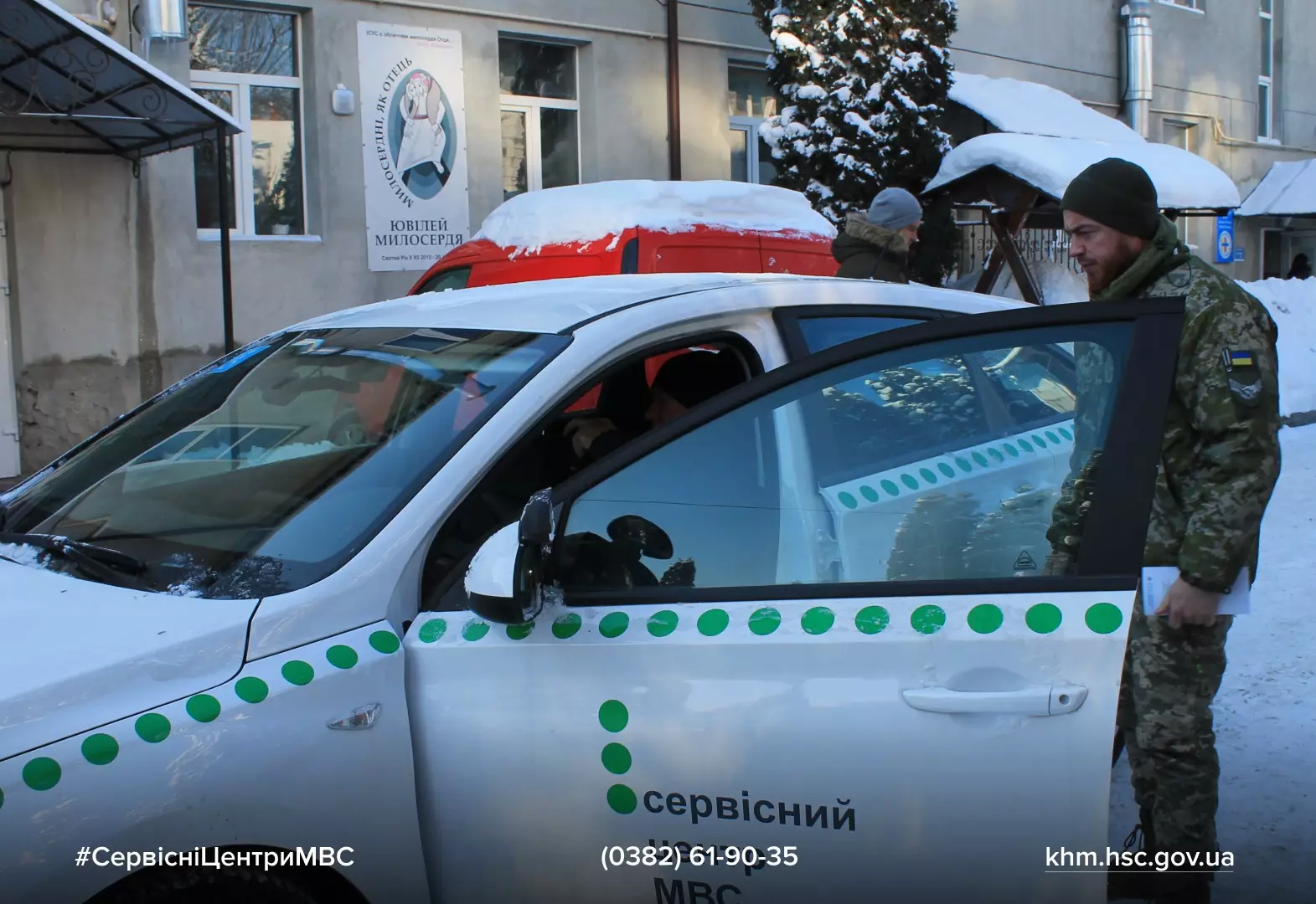 Автомобіль сервісного центру МВС, біля якого стоїть військовий, на тлі будівлі з логотипом ініціативи