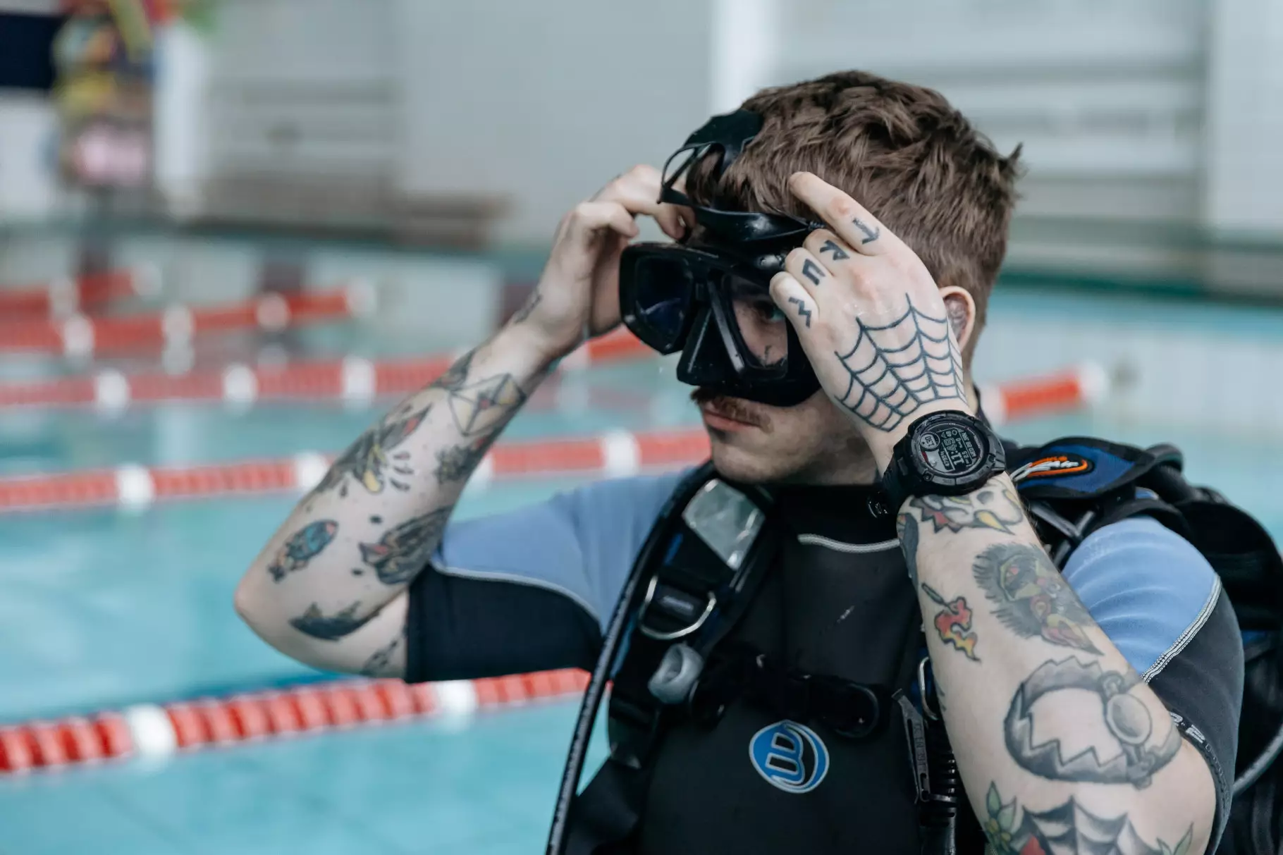 Чоловік у дайверському костюмі готується до занурення в басейні, перевіряючи маску для підводного плавання