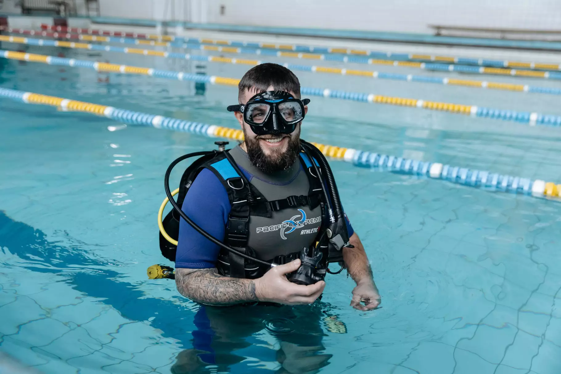 Чоловік у дайвінг-спорядженні стоїть у басейні, готуючись до занурення для реабілітації ветеранів