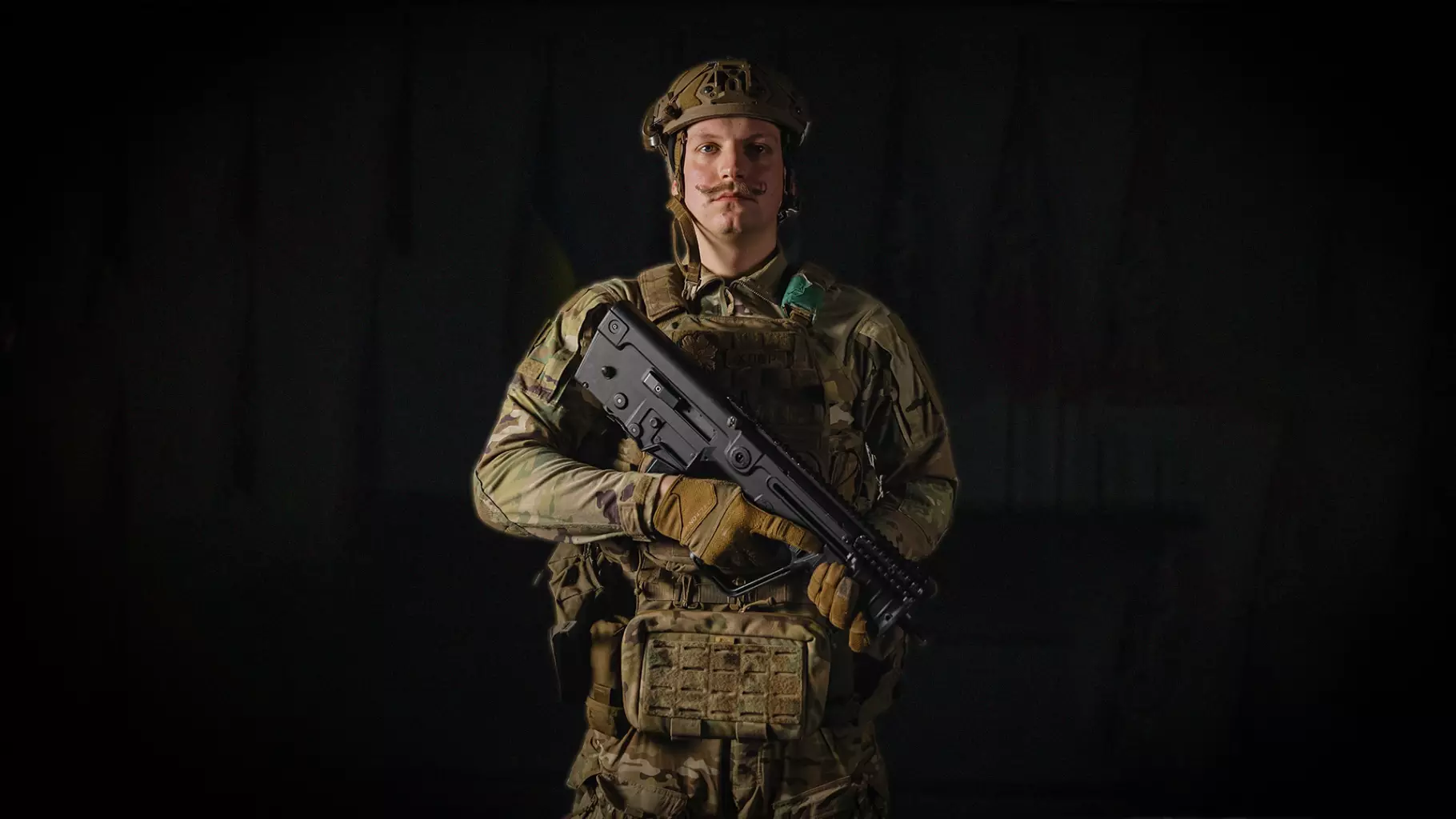 Боєць у військовій формі з автоматом, стоїть на темному фоні, символізуючи рішучість та професіоналізм