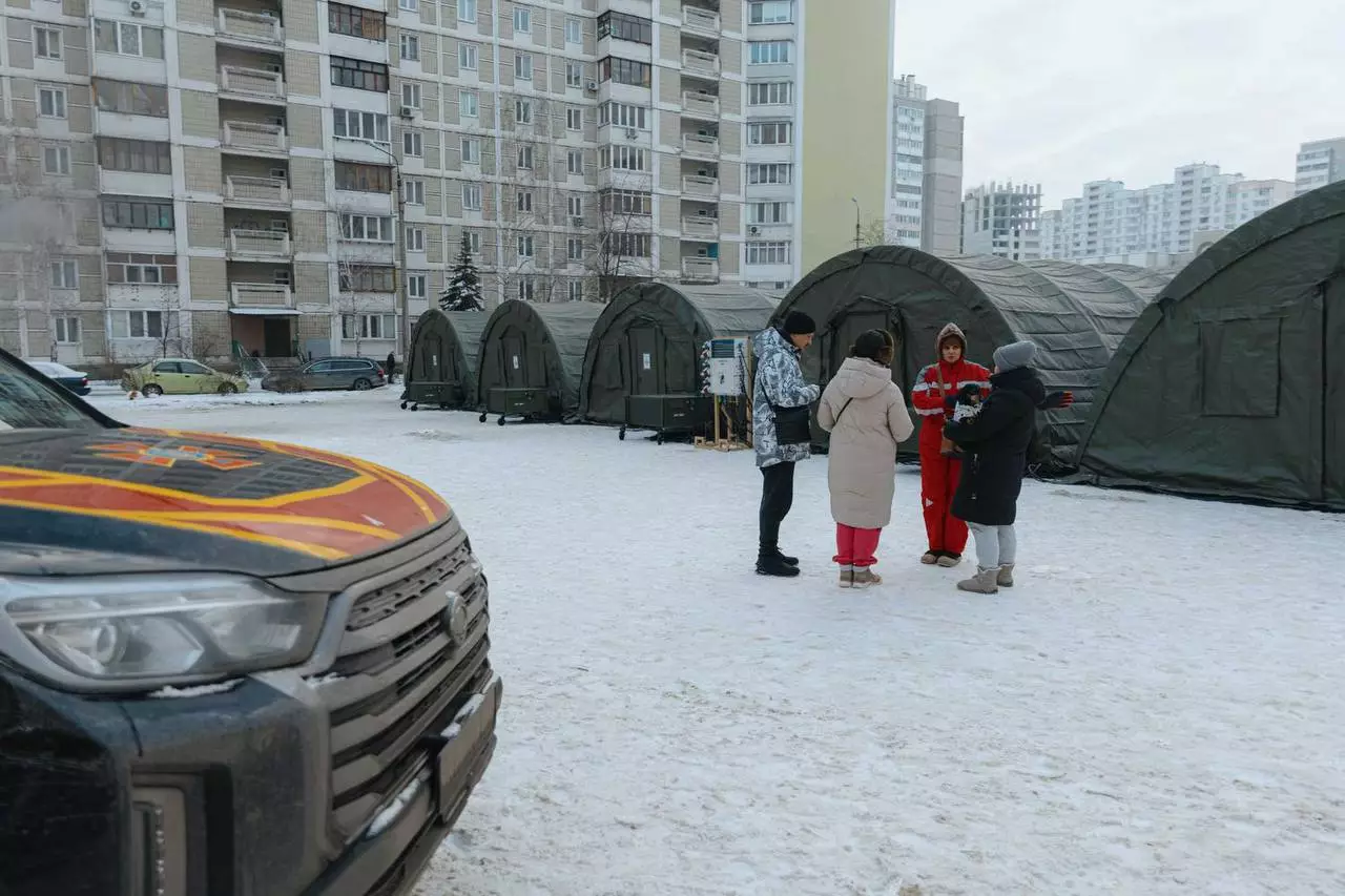 Люди біля наметів обігріву у дворі багатоповерхівки, сніг, автомобіль ДСНС на передньому плані