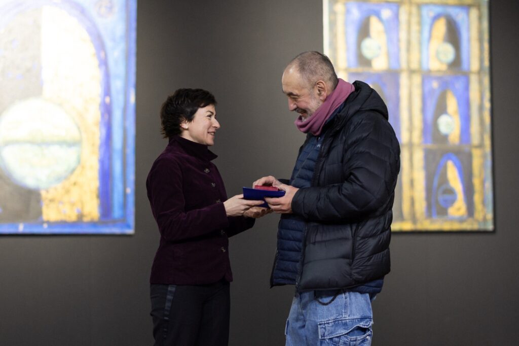 Двоє людей на виставці, одна з них вручає нагороду іншій, на стіні картини Матвія Вайсберга