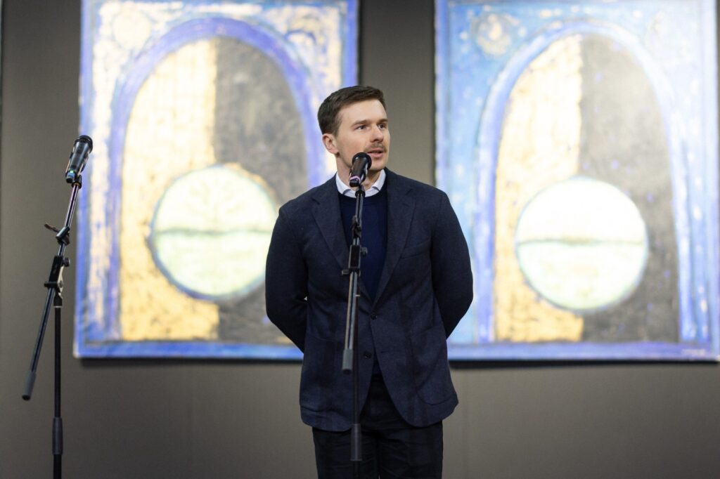 Чоловік виступає на відкритті виставки Матвія Вайсберга, на тлі мистецькі твори з синіми арками