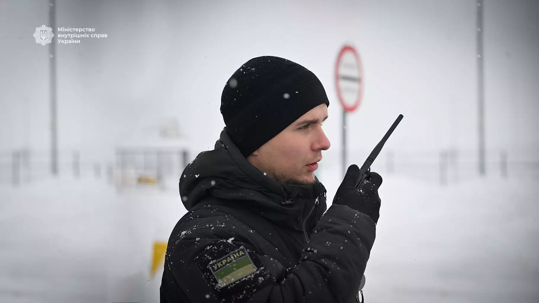 Прикордонник у зимовій формі з рацією на тлі засніженого пункту пропуску, забезпечує безпеку країни