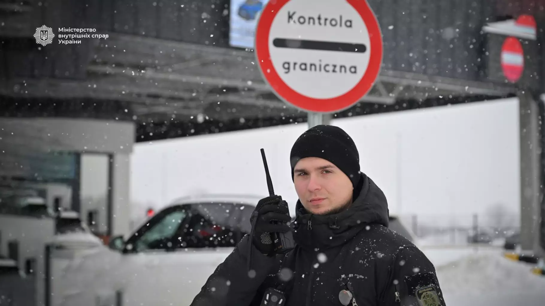 Прикордонник у зимовій формі з рацією на тлі снігу та знаку прикордонного контролю