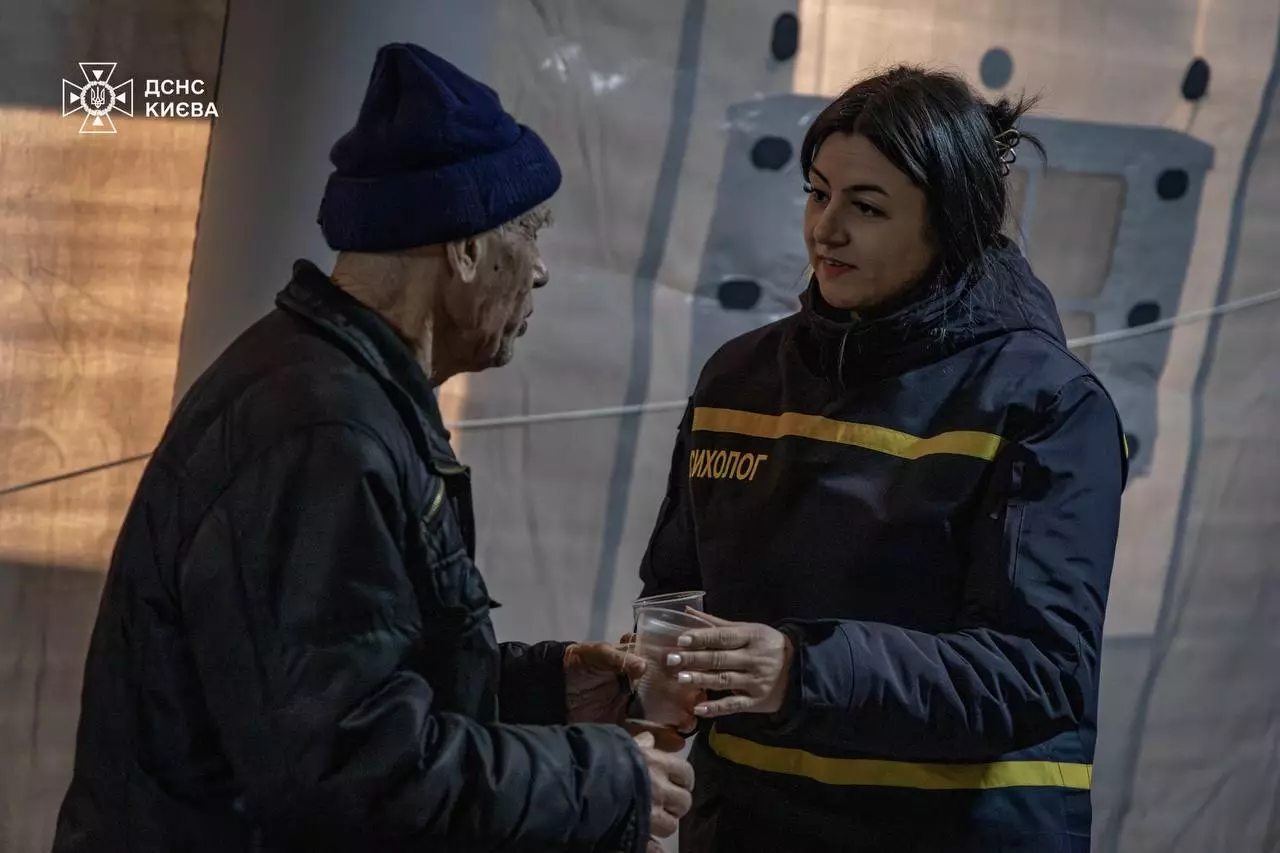 Рятувальниця ДСНС спілкується з літнім чоловіком у пункті обігріву в Києві під час кризи з теплопостачанням