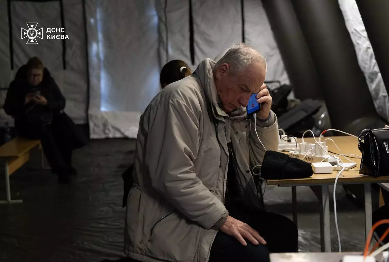 Чоловік у теплому одязі сидить у пункті незламності, заряджаючи телефон та користуючись зв'язком