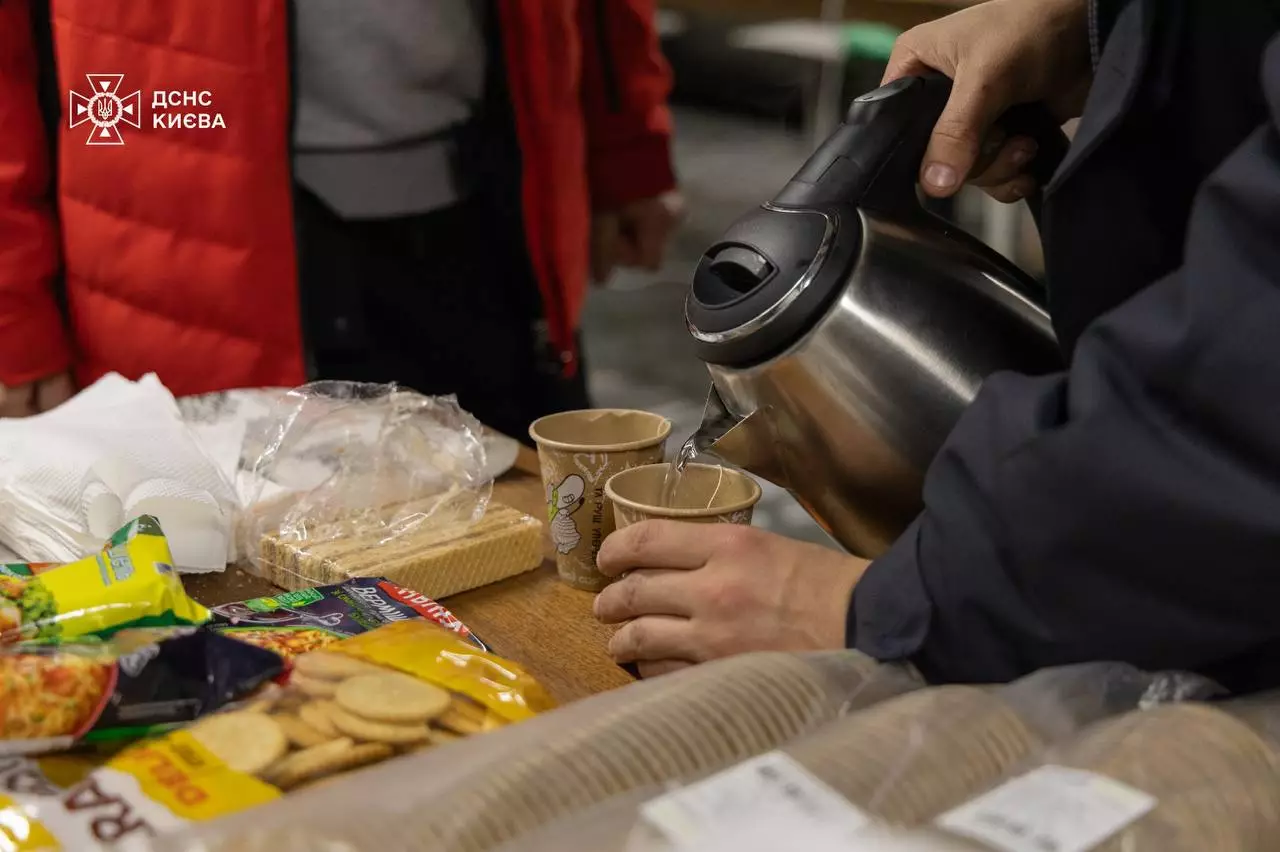 Люди наливають гарячу воду в паперові стаканчики на пункті обігріву в Києві під час кризової ситуації