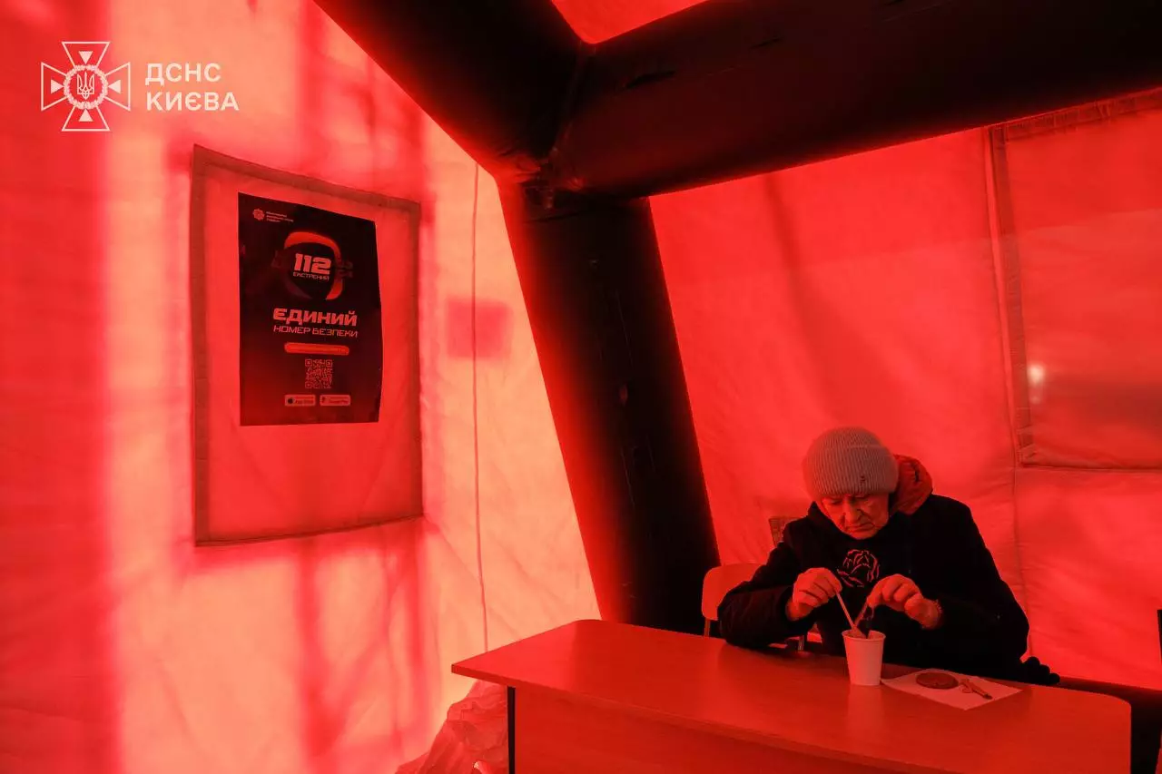 Людина в теплому наметі пункту обігріву ДСНС Києва, п'є гарячий напій під час відсутності тепла