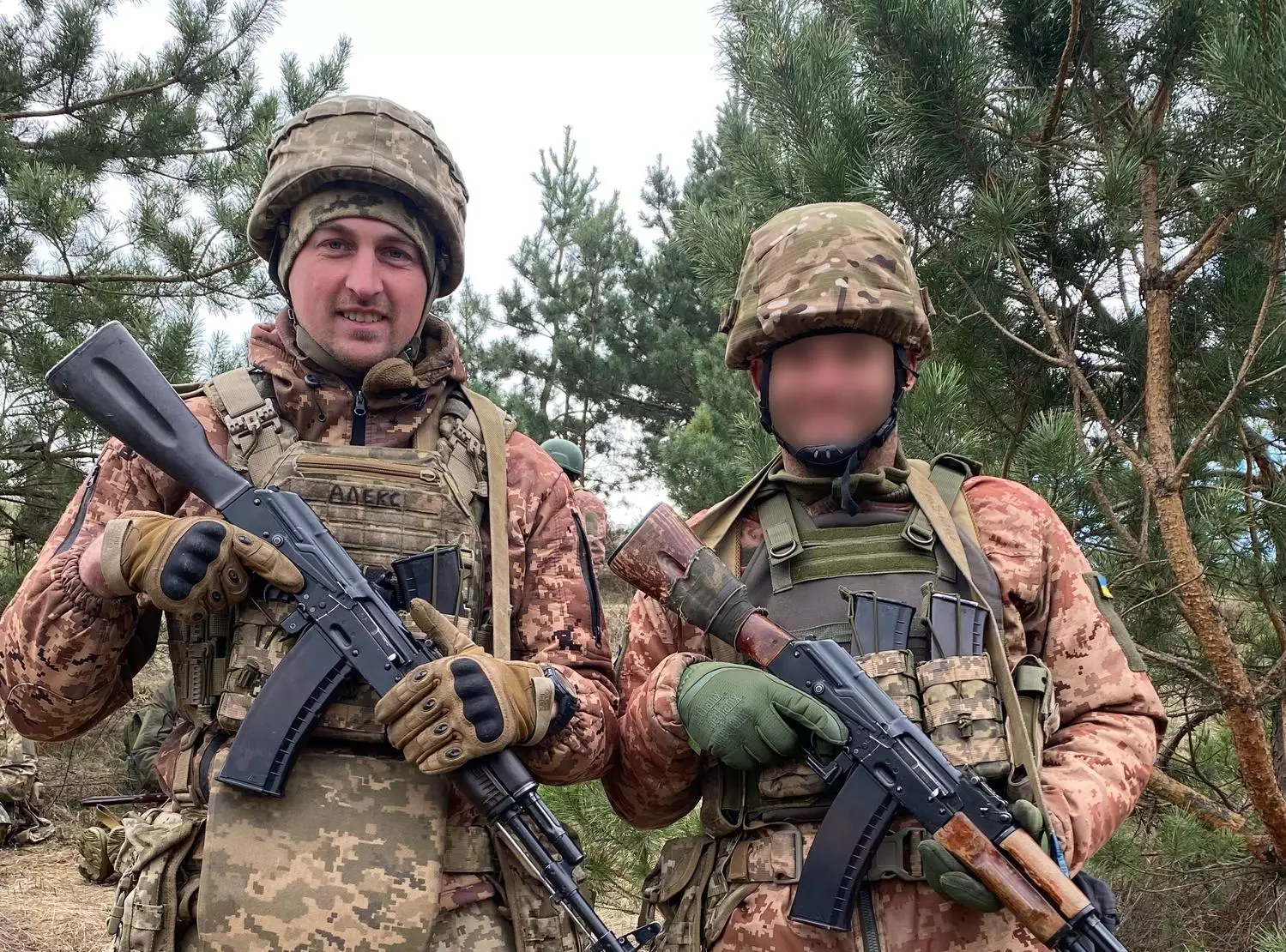 Двоє військових у камуфляжі з автоматами на фоні соснового лісу під час навчань