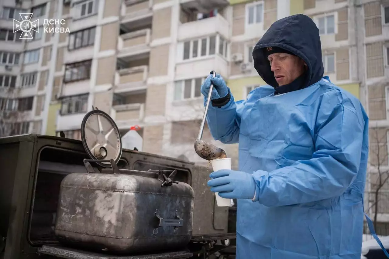 Чоловік у синьому захисному костюмі розливає гарячий напій у дворі багатоповерхівки