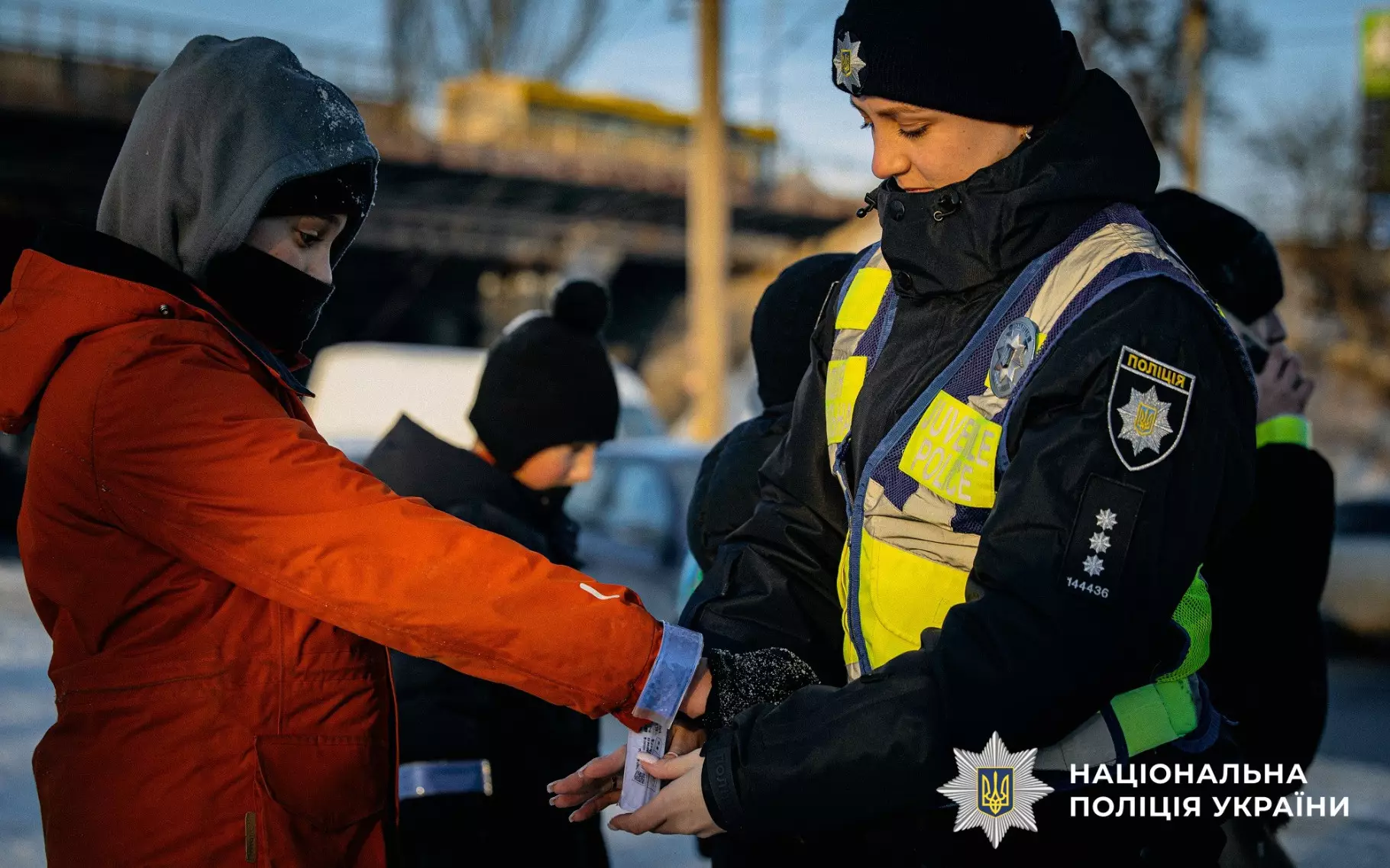 Ювенальний поліцейський на вулиці роздає дитині світловідбивальний браслет для безпеки на дорозі