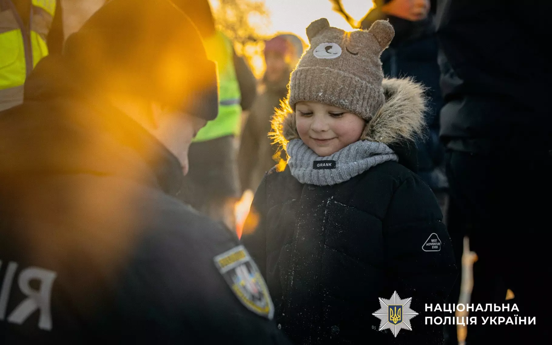 Дитина в теплому одязі отримує світловідбивальний елемент від поліцейського на вулиці взимку