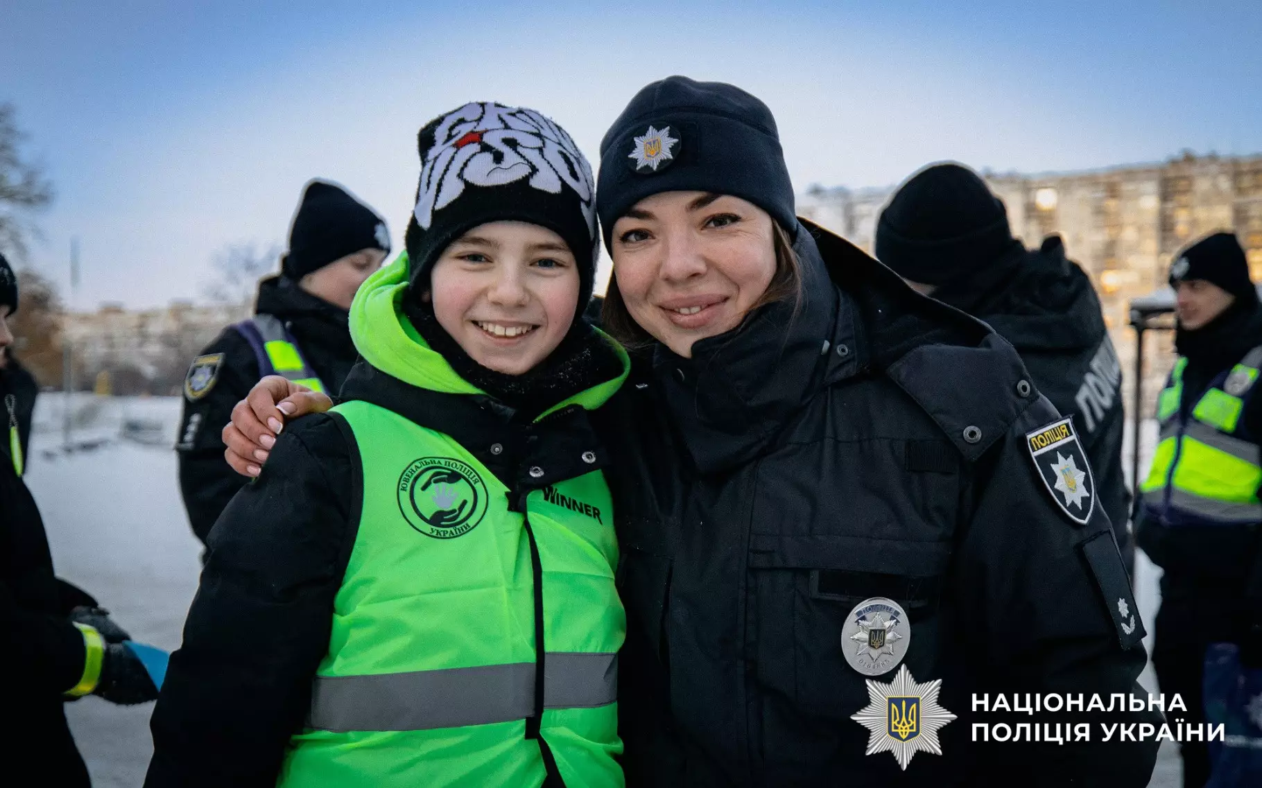 Ювенальний поліцейський обіймає дитину у світловідбивальному жилеті на зимовій вулиці