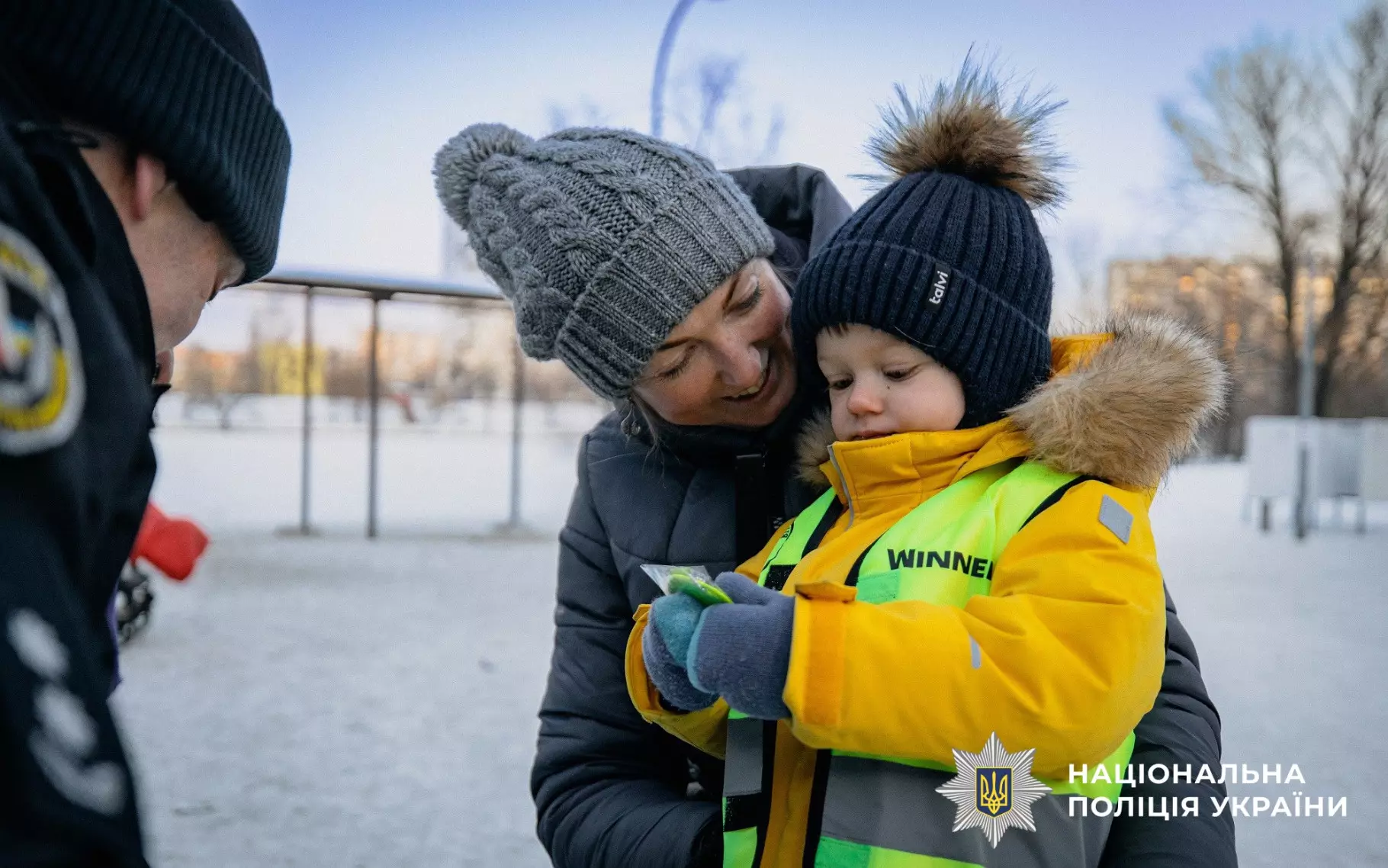 Дитина в жовтому жилеті зі світловідбивальними елементами на зимовій прогулянці з поліцейськими