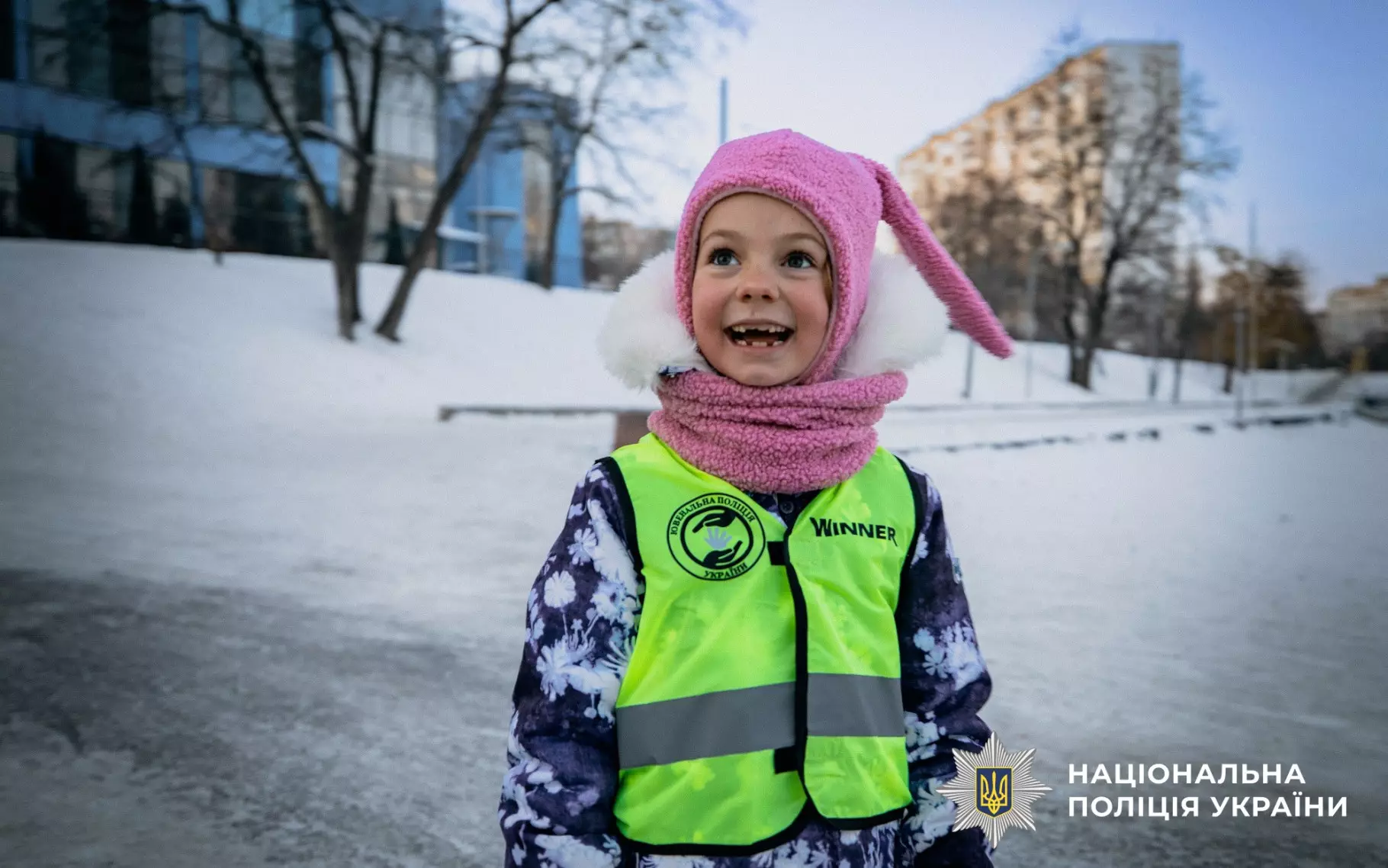 Дитина в яскравому жилеті зі світловідбивальними елементами на зимовій прогулянці в місті