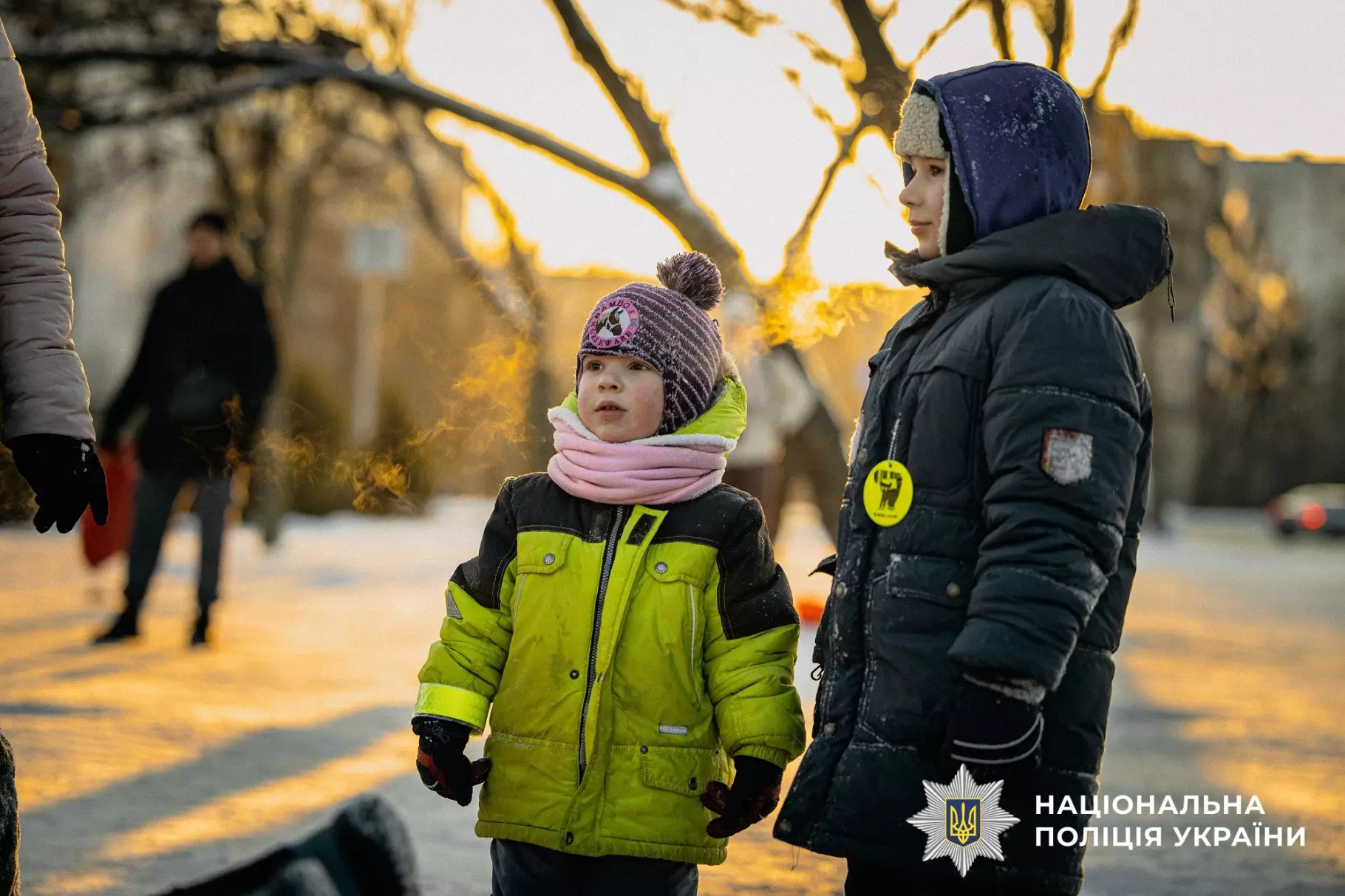 Діти в зимовому одязі на вулиці, один з них у світловідбивальному жилеті, поруч поліцейський значок