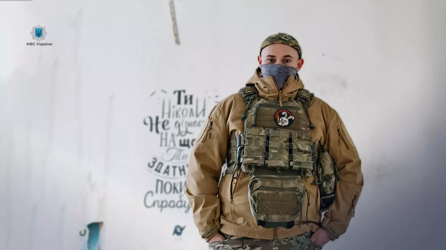 Прикордонник у військовій формі стоїть на тлі стіни з патріотичним написом