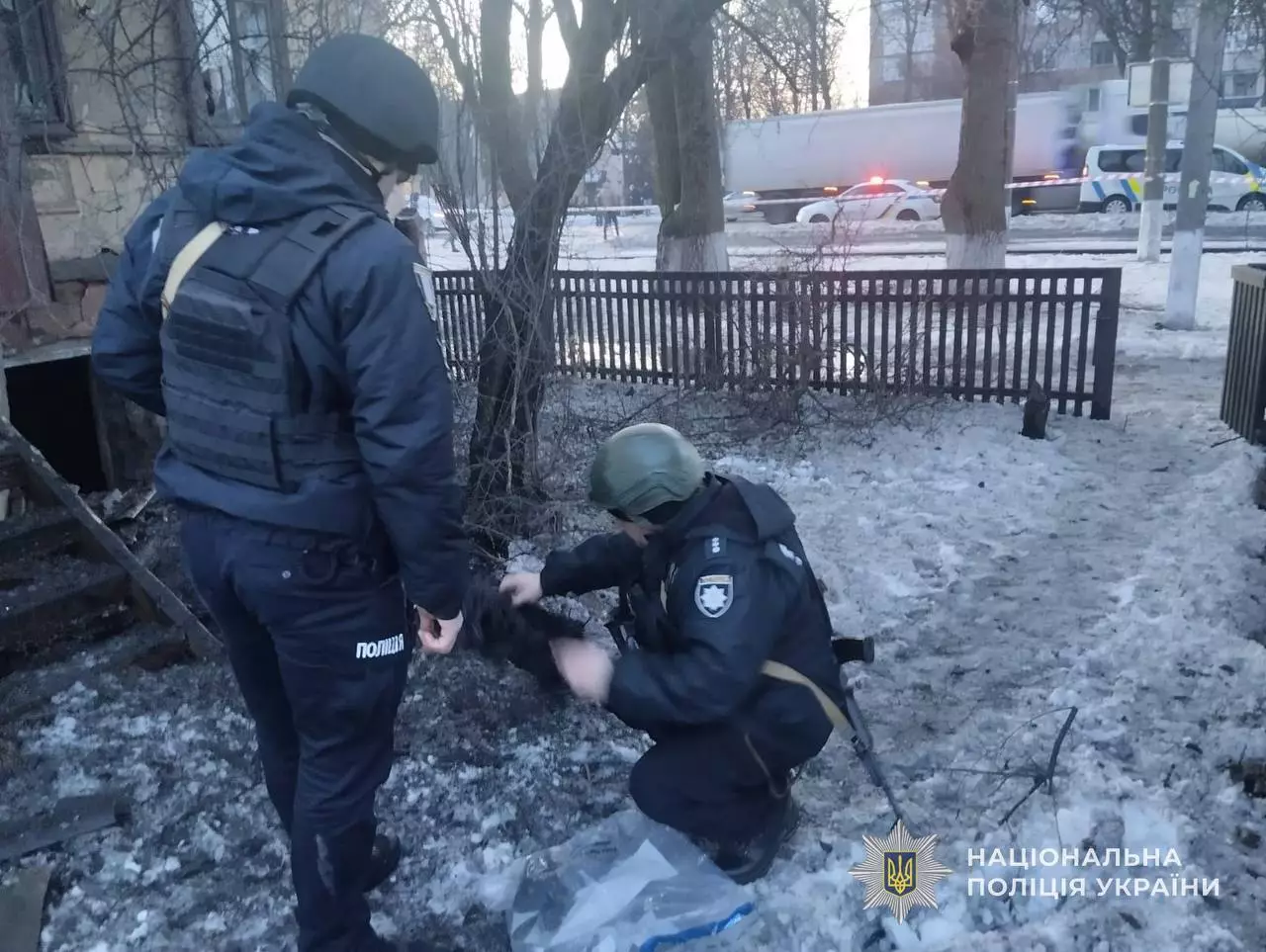 Поліцейські в захисному спорядженні оглядають місце обстрілу в зимовому парку на Київщині