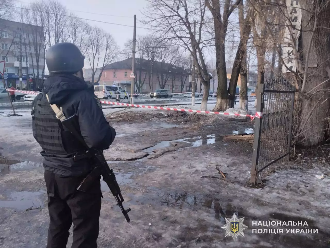 Поліцейський з автоматом на місці обстрілу, огороджене стрічкою, зимовий пейзаж, дерева без листя