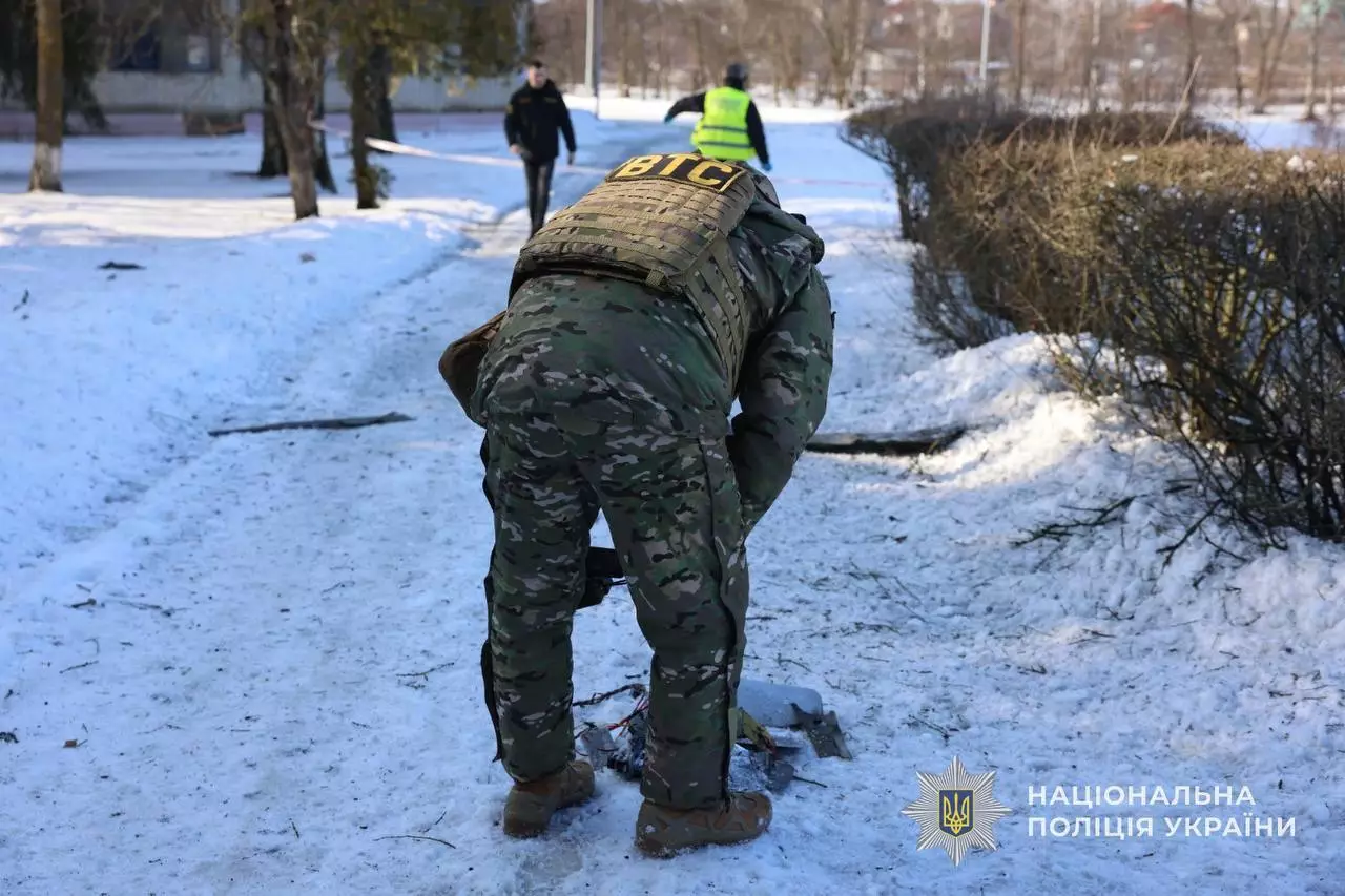 Поліцейський у камуфляжі оглядає уламки на засніженій вулиці після обстрілу в Україні