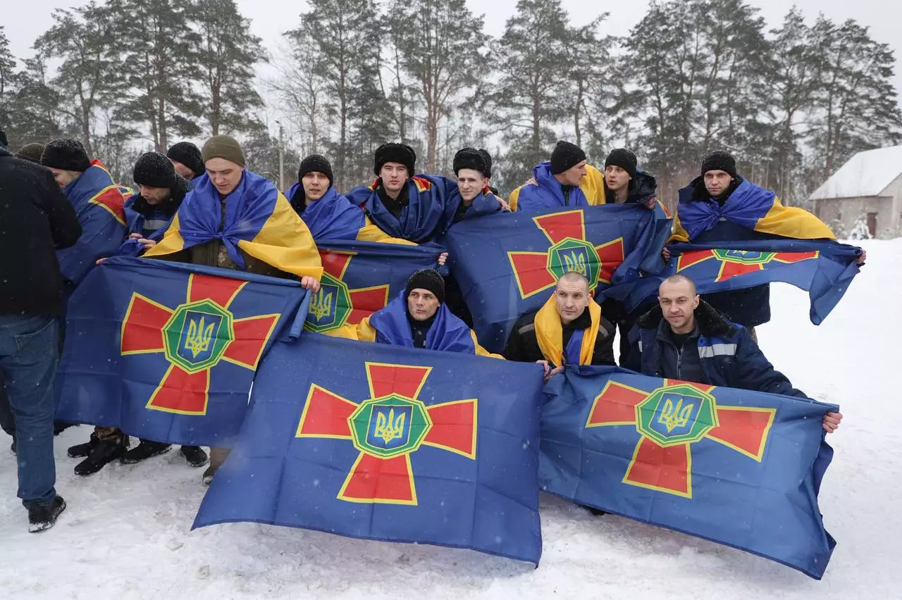 Група військових у зимовому одязі з прапорами України на снігу, повернення з полону