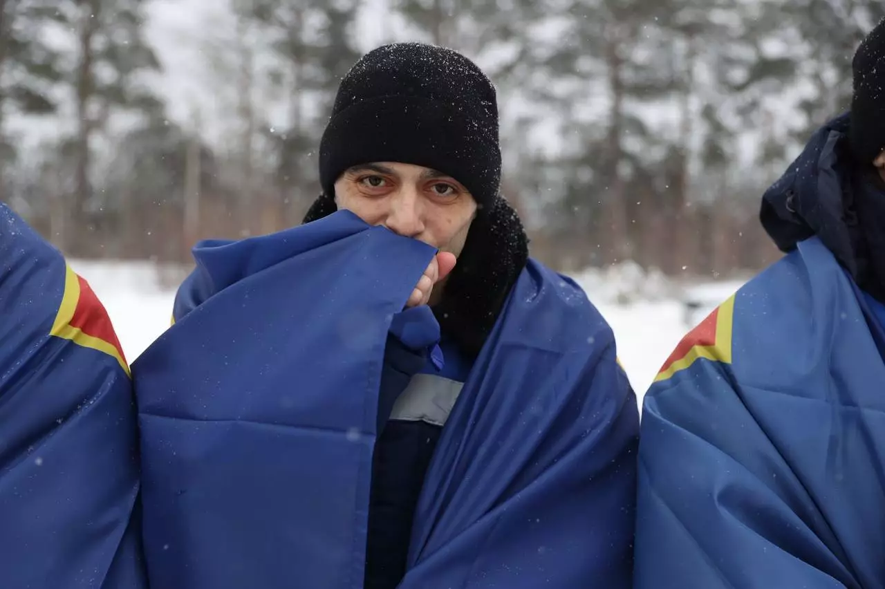 Троє військових у зимовому одязі, загорнуті в сині ковдри, стоять на снігу на тлі засніженого лісу