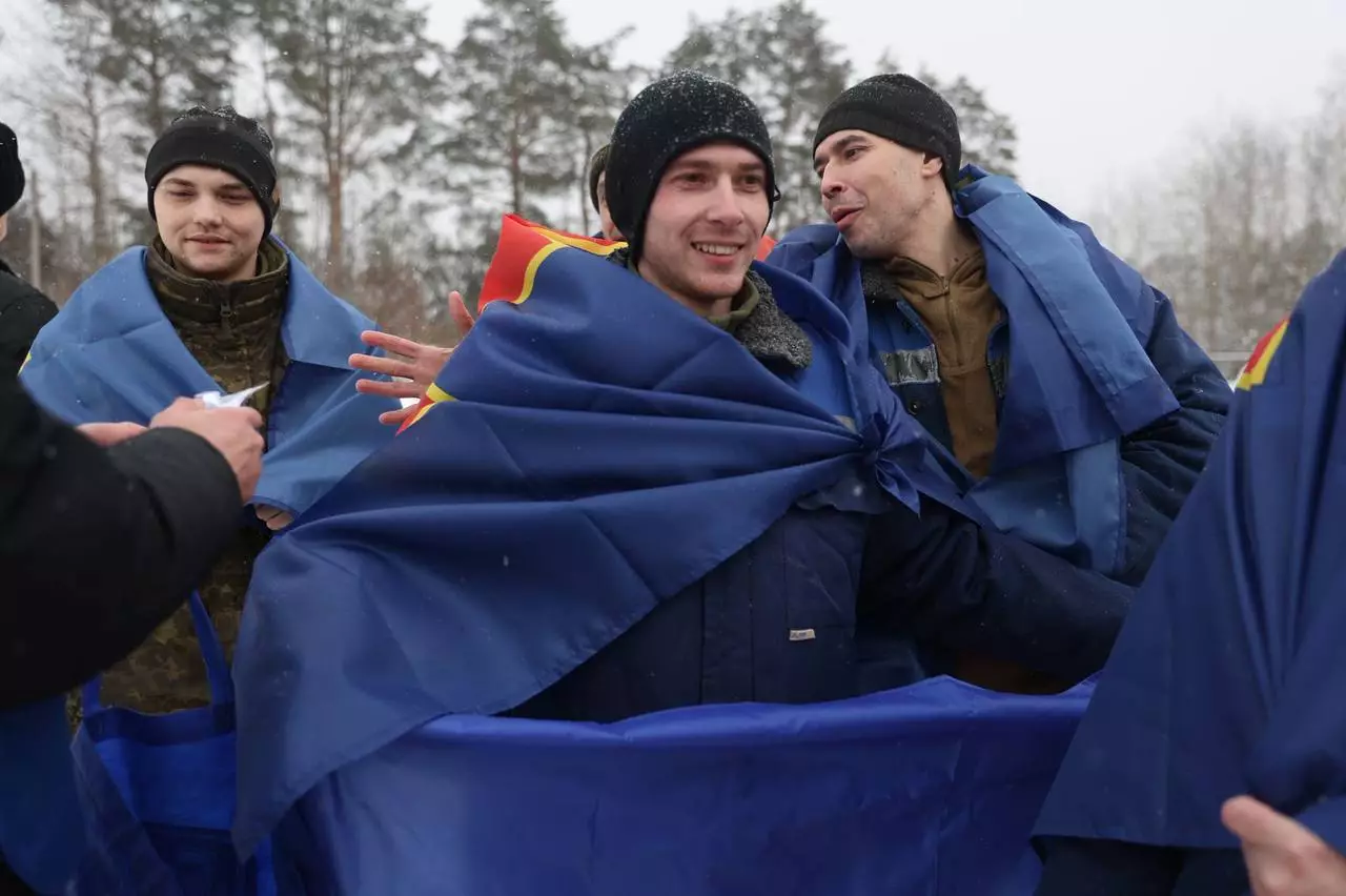 Троє чоловіків, загорнуті в сині прапори, радісно обіймаються на тлі зимового пейзажу