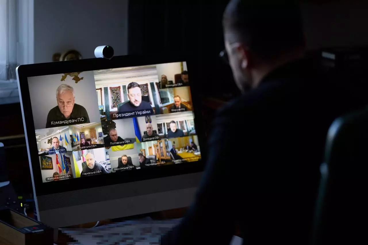 Чоловік дивиться на екран комп'ютера з відеоконференцією за участю Президента України та урядовців