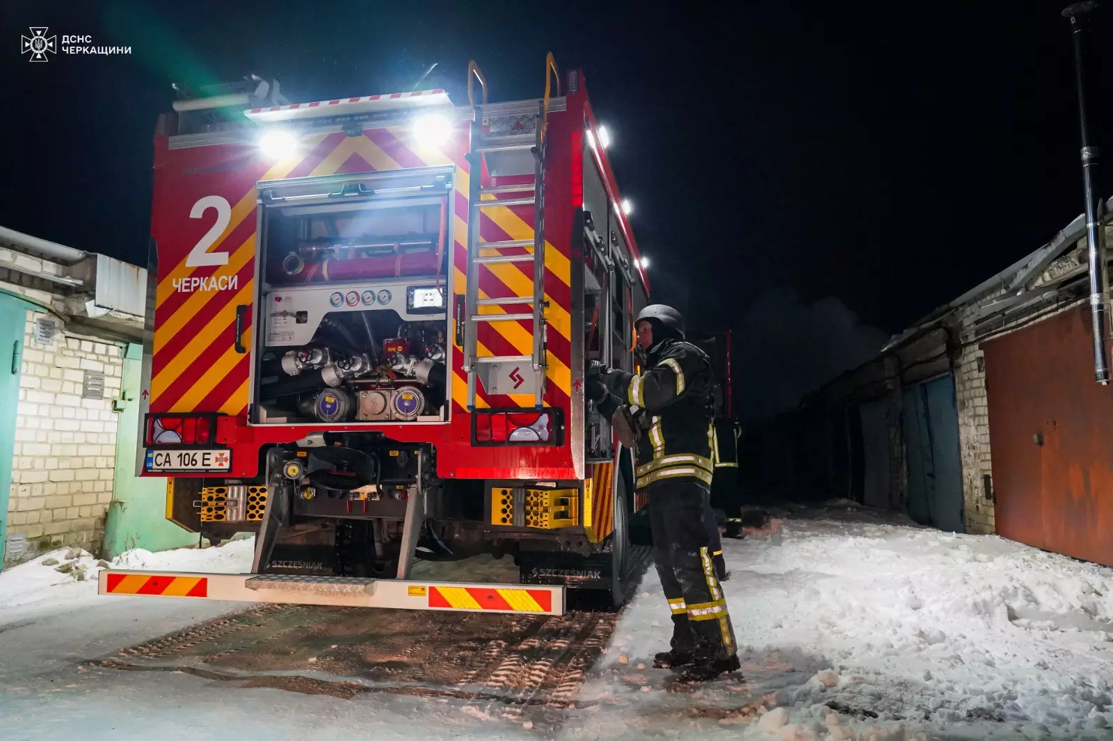Рятувальник біля пожежної машини на засніженій вулиці вночі після обстрілів у Черкасах
