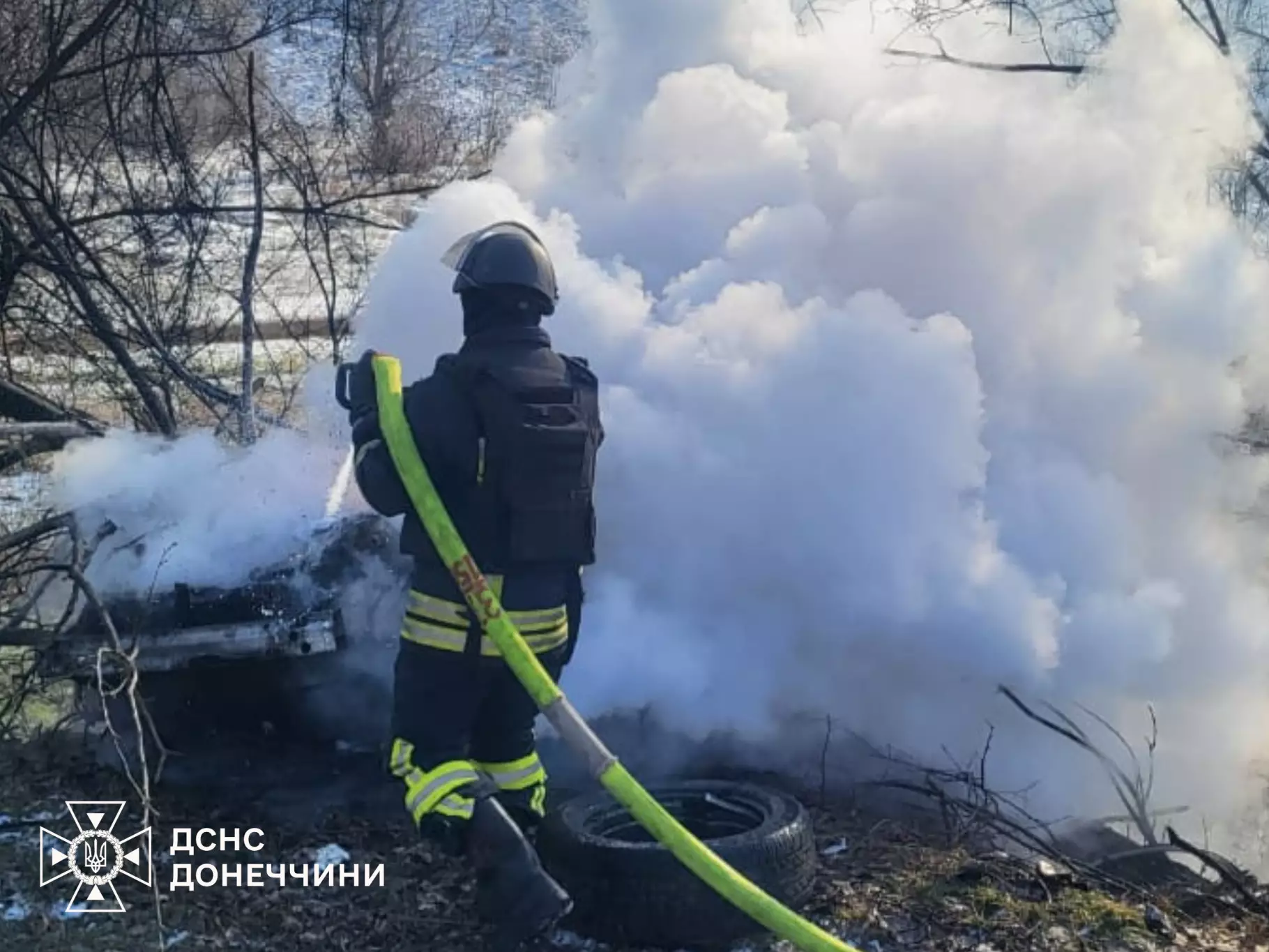 Рятувальник гасить пожежу після обстрілу, густий дим піднімається вгору, пошкоджені дерева навколо