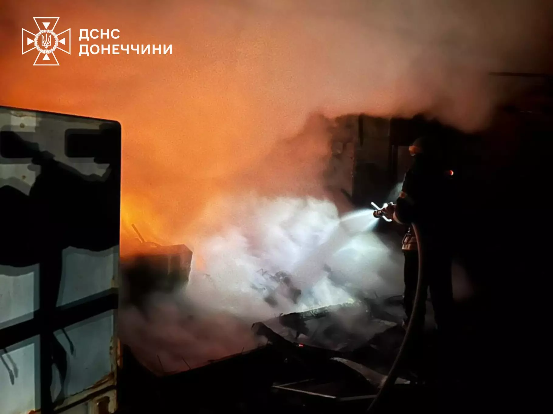 Рятувальник гасить пожежу серед диму вночі, наслідки обстрілів у Донеччині