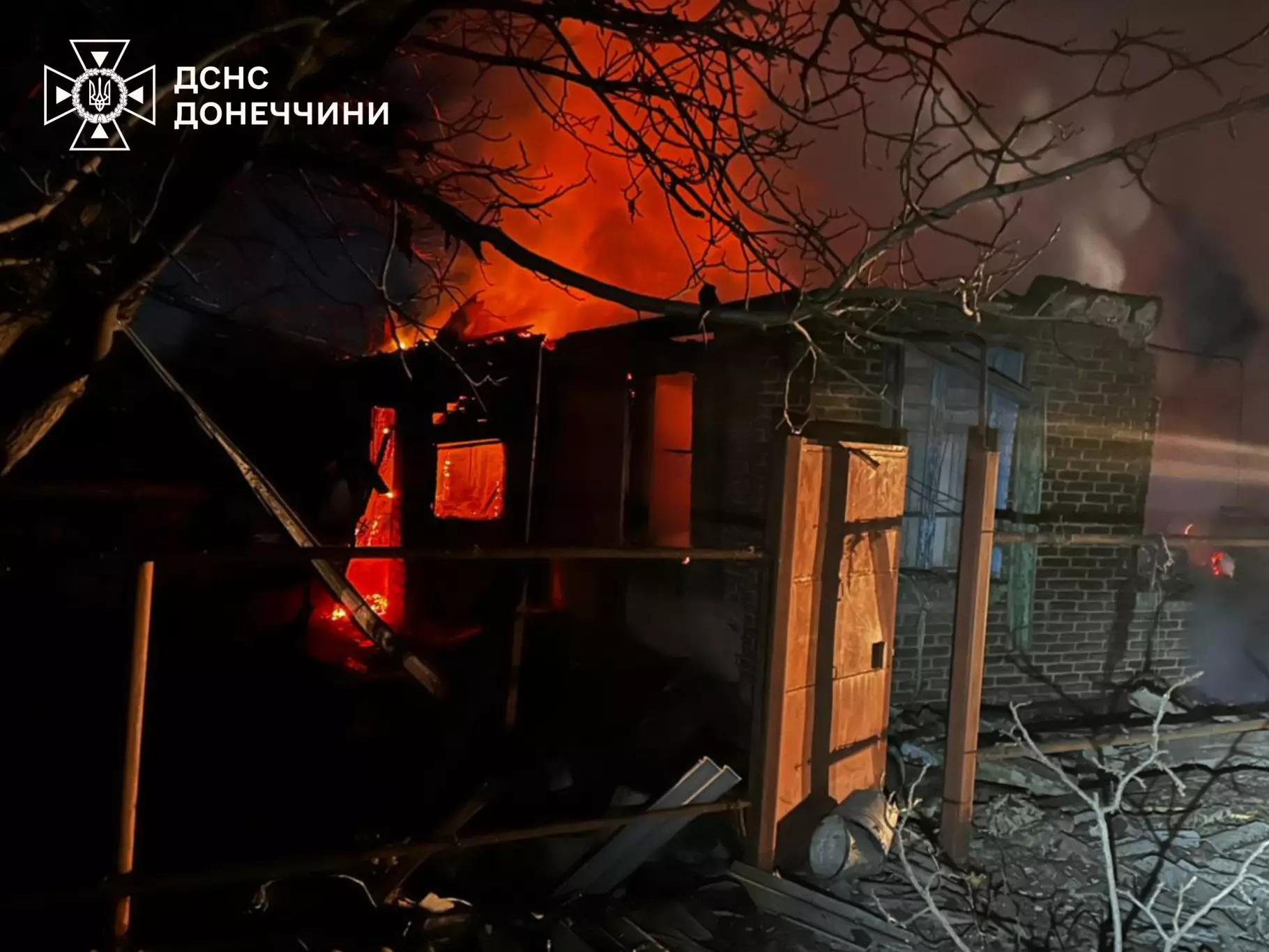 Палаючий будинок після обстрілу, вогонь охопив дах, навколо розкидані уламки, нічний час