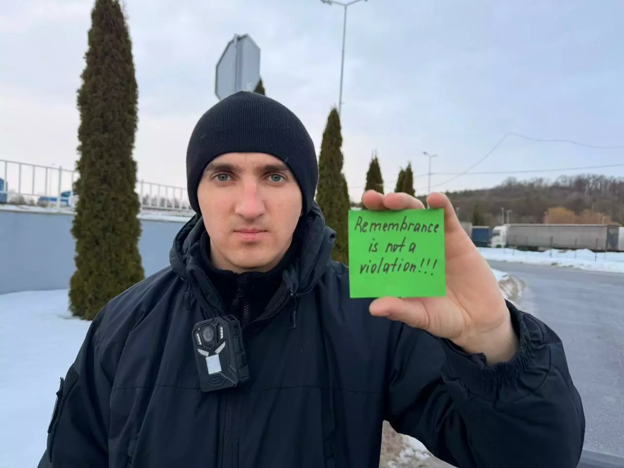 Чоловік у формі тримає табличку з написом "Remembrance is not a violation" на вулиці взимку