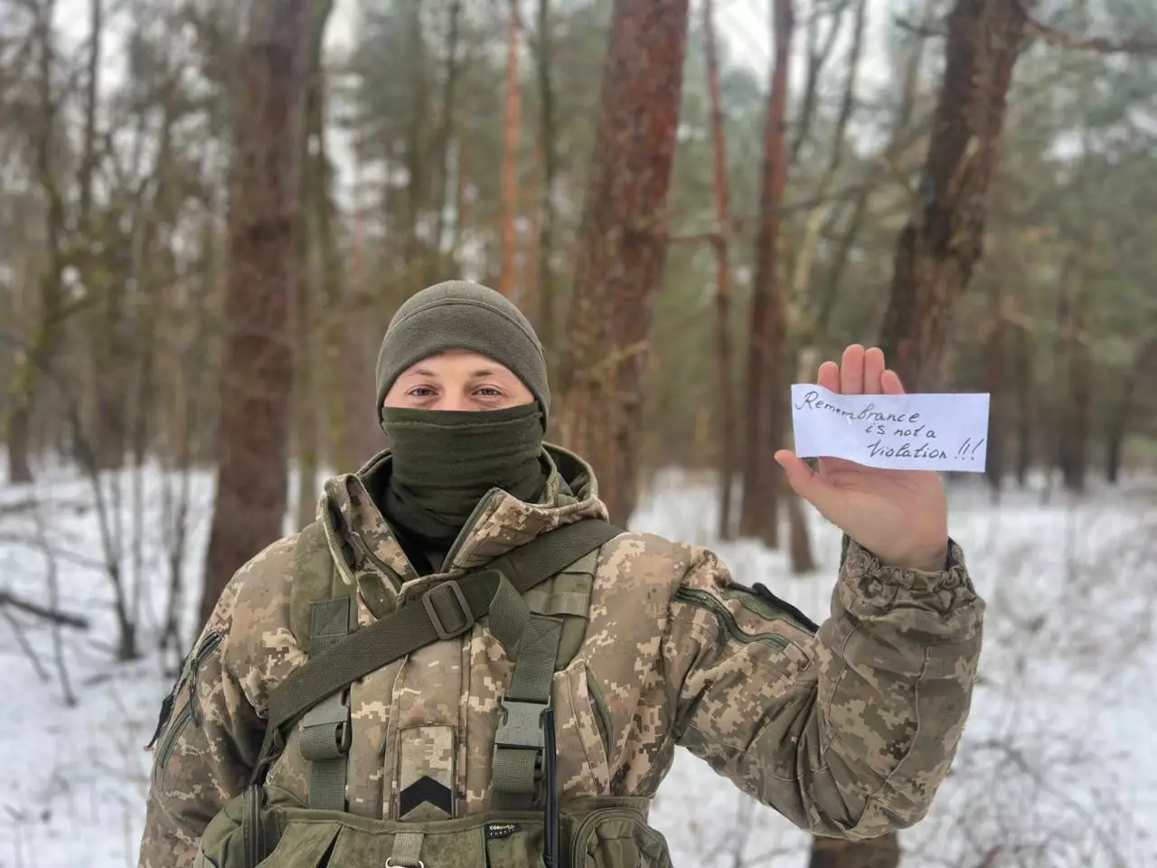 Військовослужбовець у зимовому лісі тримає напис "Remembrance is not a violation