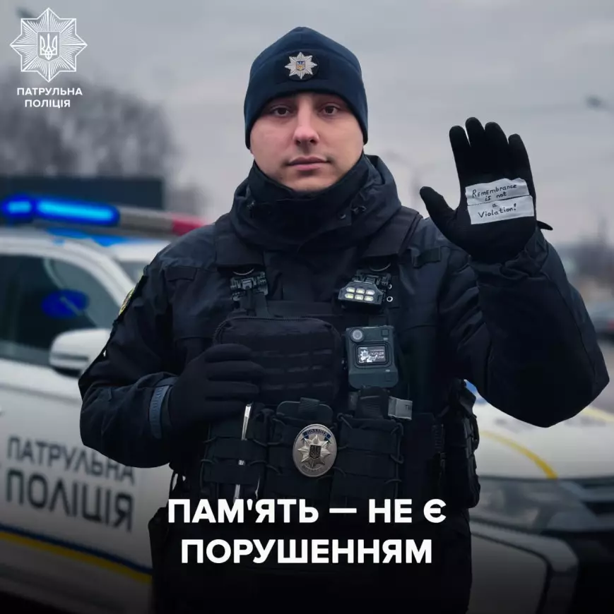 Поліцейський у формі тримає руку з написом "Пам'ять — не є порушенням" на фоні патрульного авто