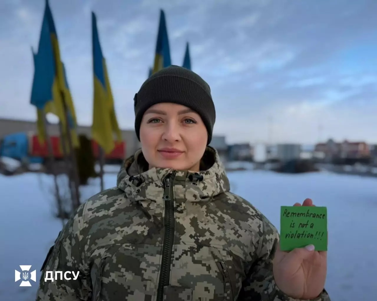 Військовослужбовець ДПСУ у формі тримає табличку з написом, на фоні українські прапори