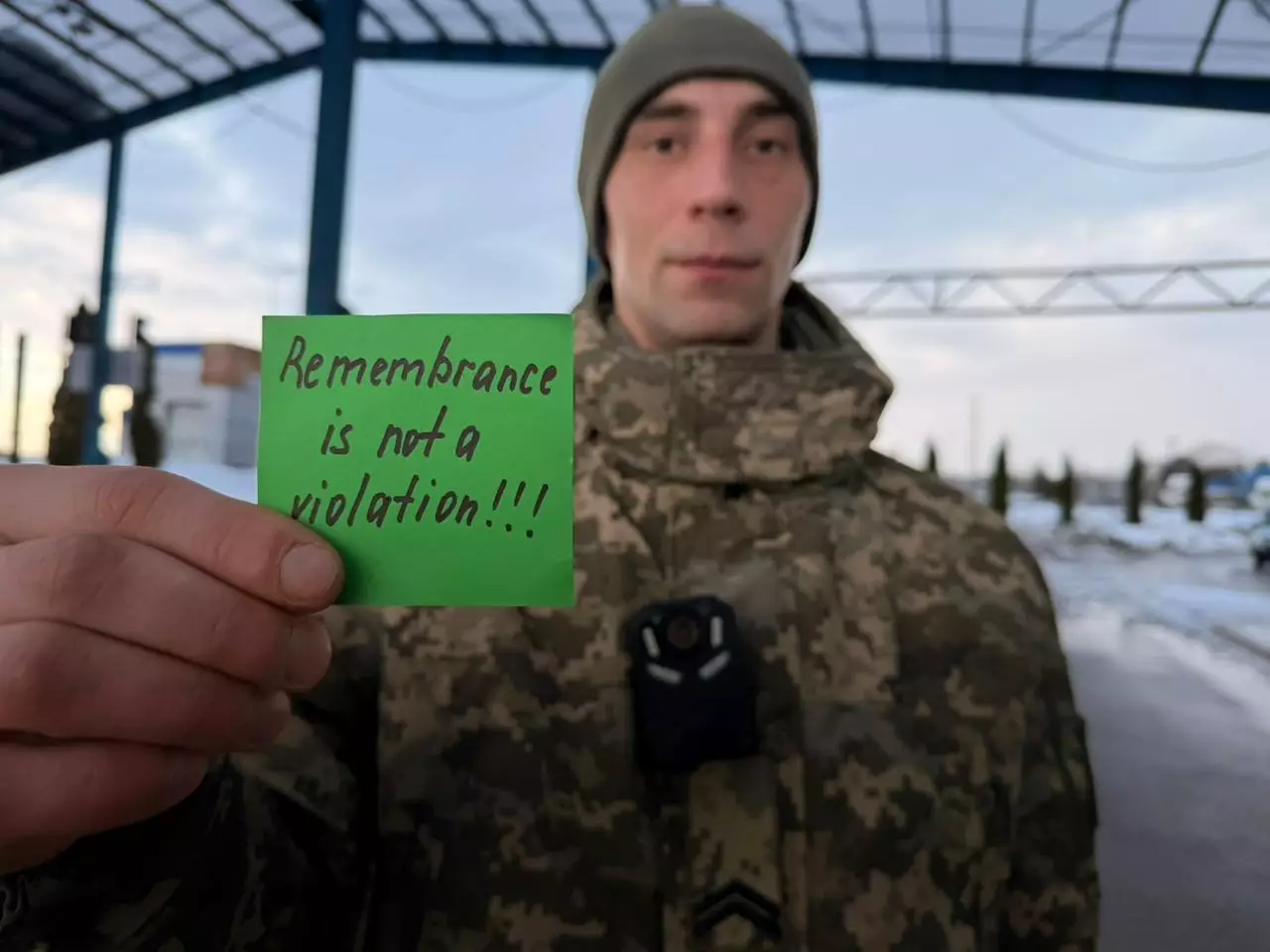 Військовослужбовець у формі тримає зелений папірець з написом "Remembrance is not a violation