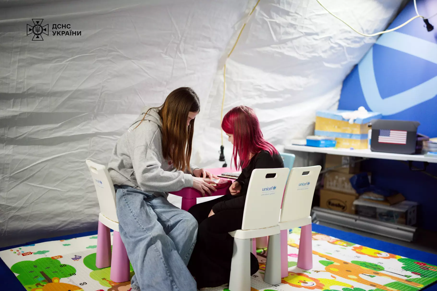 Діти займаються творчістю в мобільному пункті незламності ДСНС та ЮНІСЕФ, сидячи за столиком