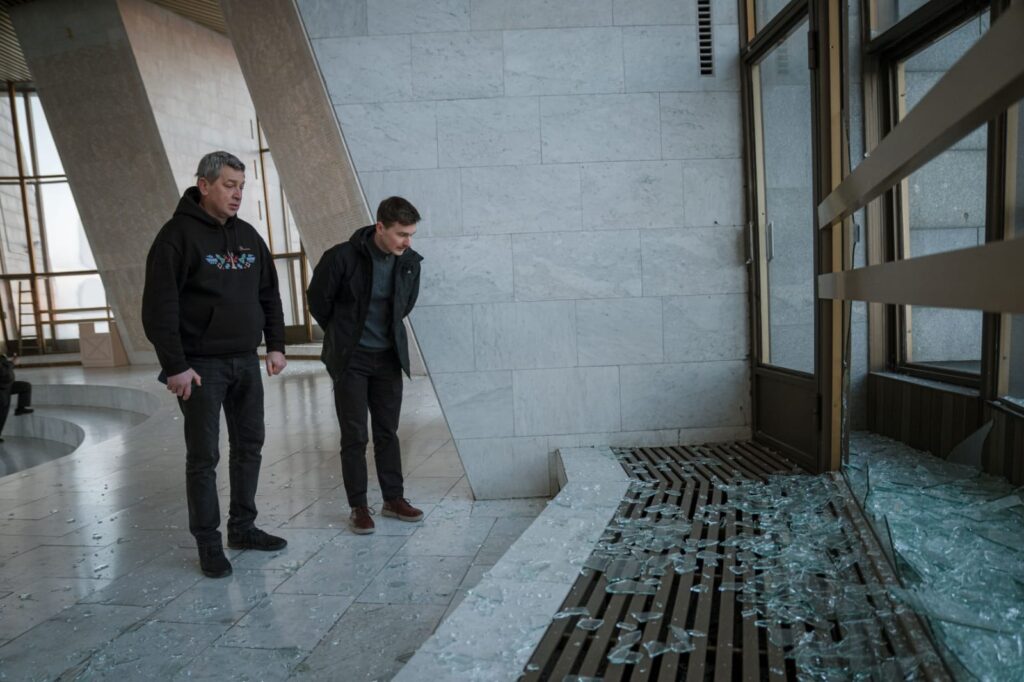 Двоє чоловіків оглядають розбиті вікна та уламки скла в залі музею після ракетного обстрілу