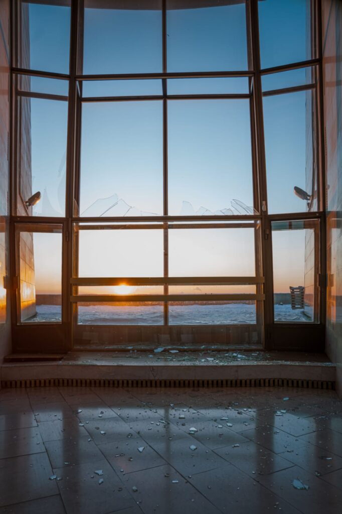 Зруйноване вікно музею з видом на захід сонця, уламки скла на підлозі після обстрілу