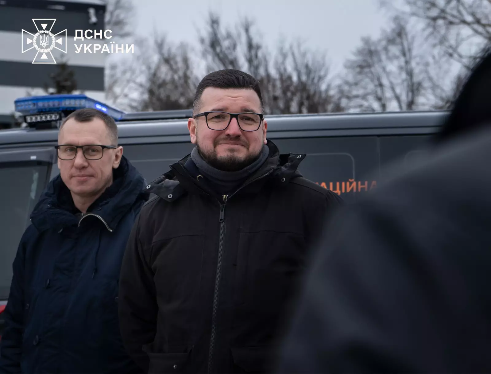 Двоє чоловіків стоять перед броньованим Volkswagen Transporter з логотипом ДСНС України на фоні