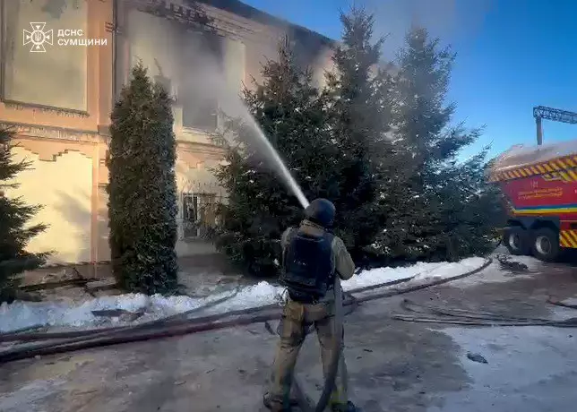 Рятувальник гасить пожежу біля будівлі після обстрілу в Україні, дим піднімається в небо