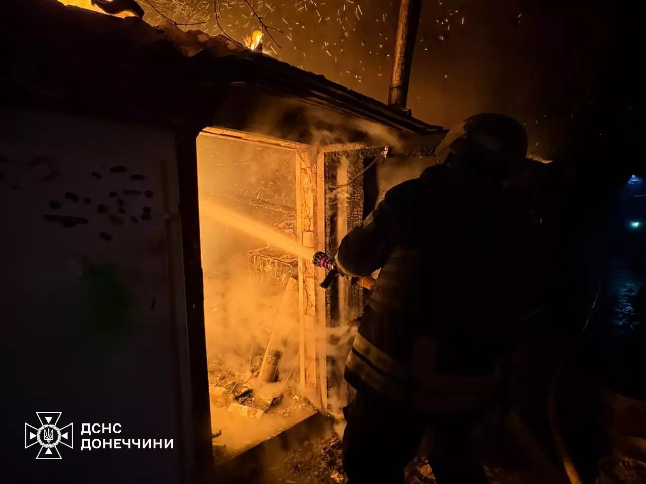 Пожежник гасить вогонь у будівлі вночі, іскри летять у повітрі, пожежа внаслідок обстрілів