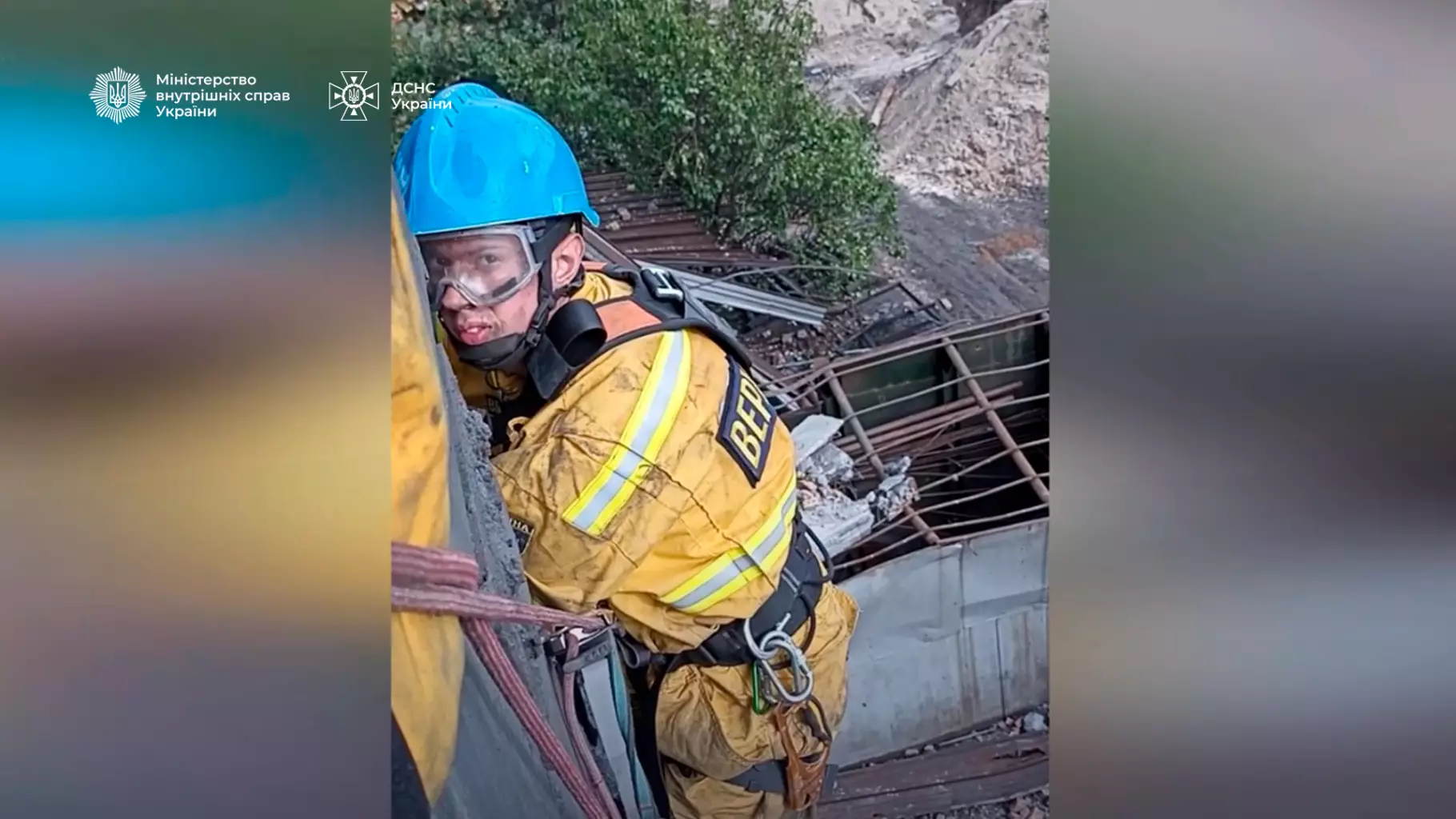 Рятувальник у жовтому костюмі та синій касці виконує роботи на висоті біля зруйнованої будівлі