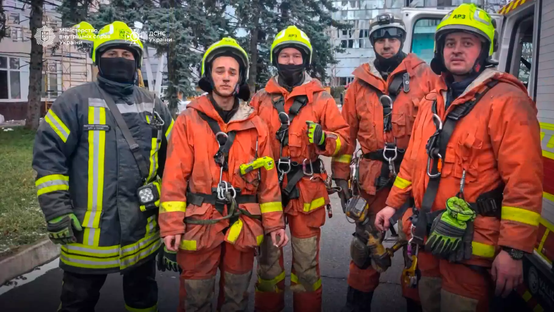 Рятувальники ДСНС у захисному спорядженні стоять перед пожежною машиною на фоні міської забудови